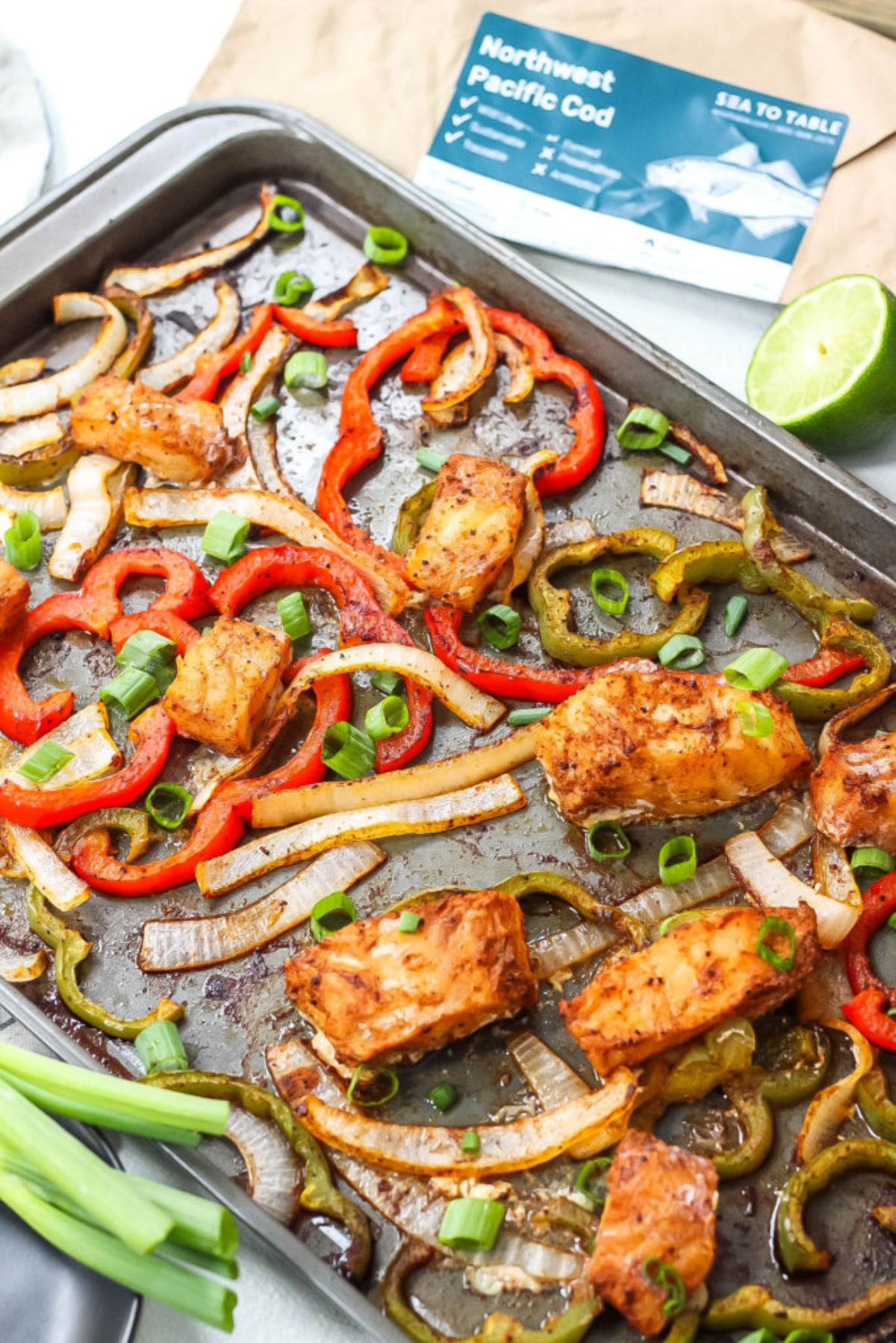 a sheet pan of fish, sliced peppers, scallions, and onions