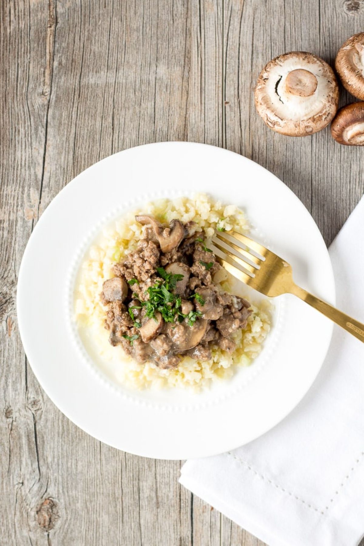 A white plate with beef stroganoff topped with choppd herbs and a goldern fork