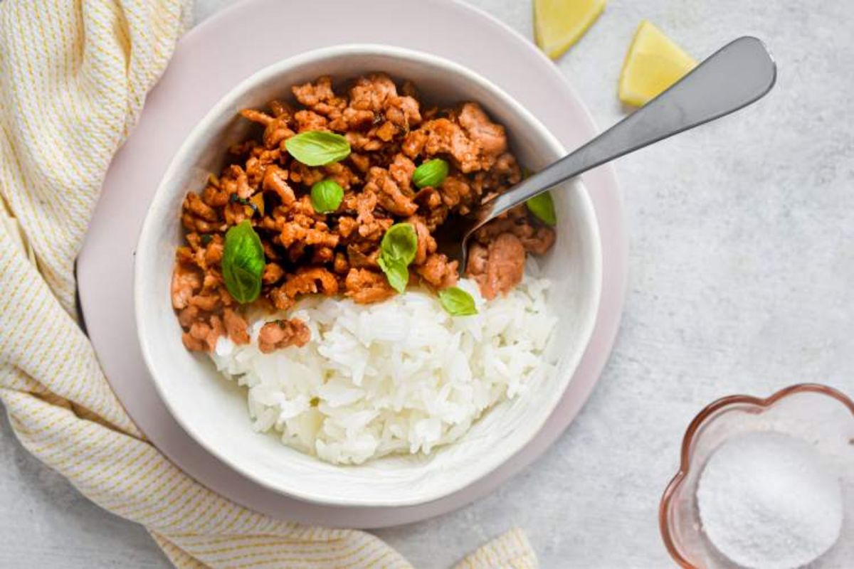 A white bowl of ground turkey and rice with basil lieaves sprinkled on top and a spook sticking out of the mixture