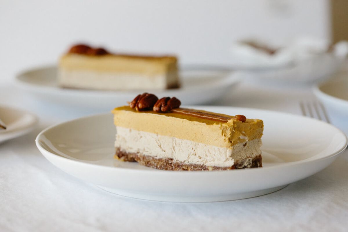 2 white plates with layered cheesecake bars topped with halved pecans