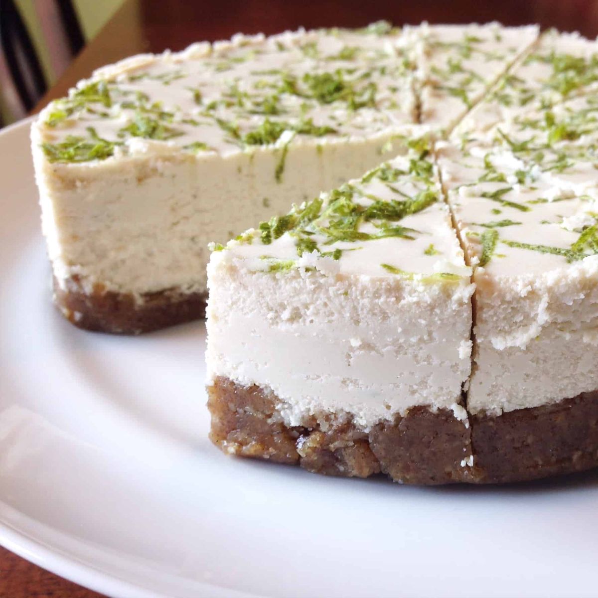 a key lime cheesecake cut into segments, with one missing. Lime zest is sprinkled on top