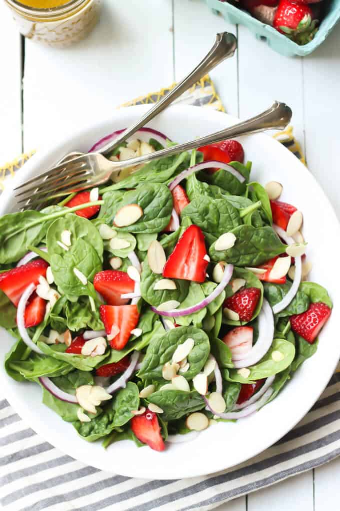 strawberry spinach salad with poppy seed dressing on a white plate with forks