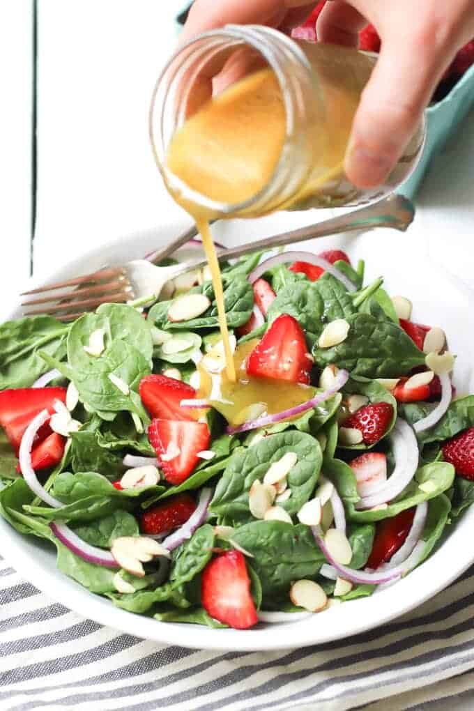 easy strawberry spinach salad with poppy seed dressing pouring out of jar