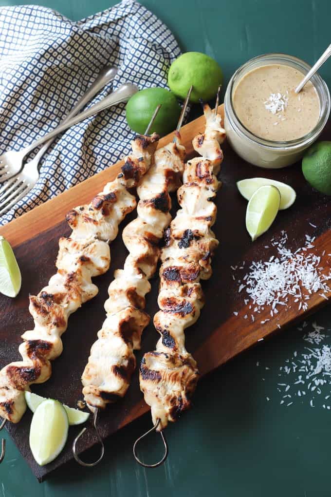 grilled Thai chicken satay skewers on a cutting board with limes