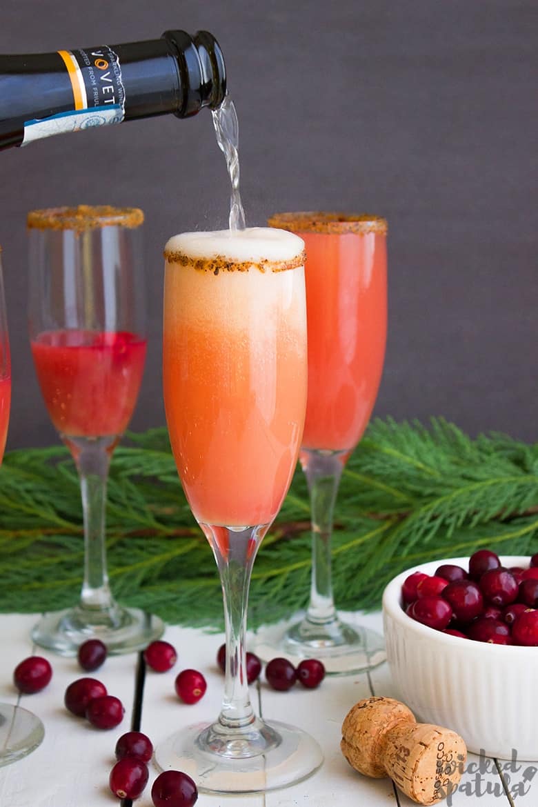 pouring prosecco into mimosa with cranberry juice 