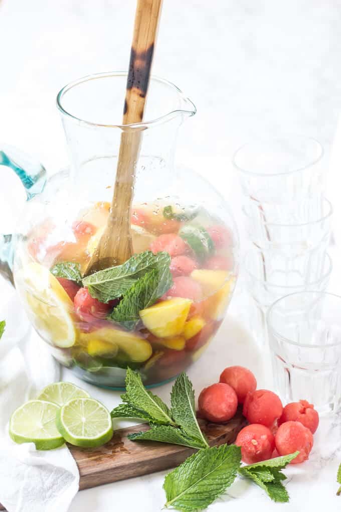 peach sangria in a pitcher with limes, mint and watermelon garnish