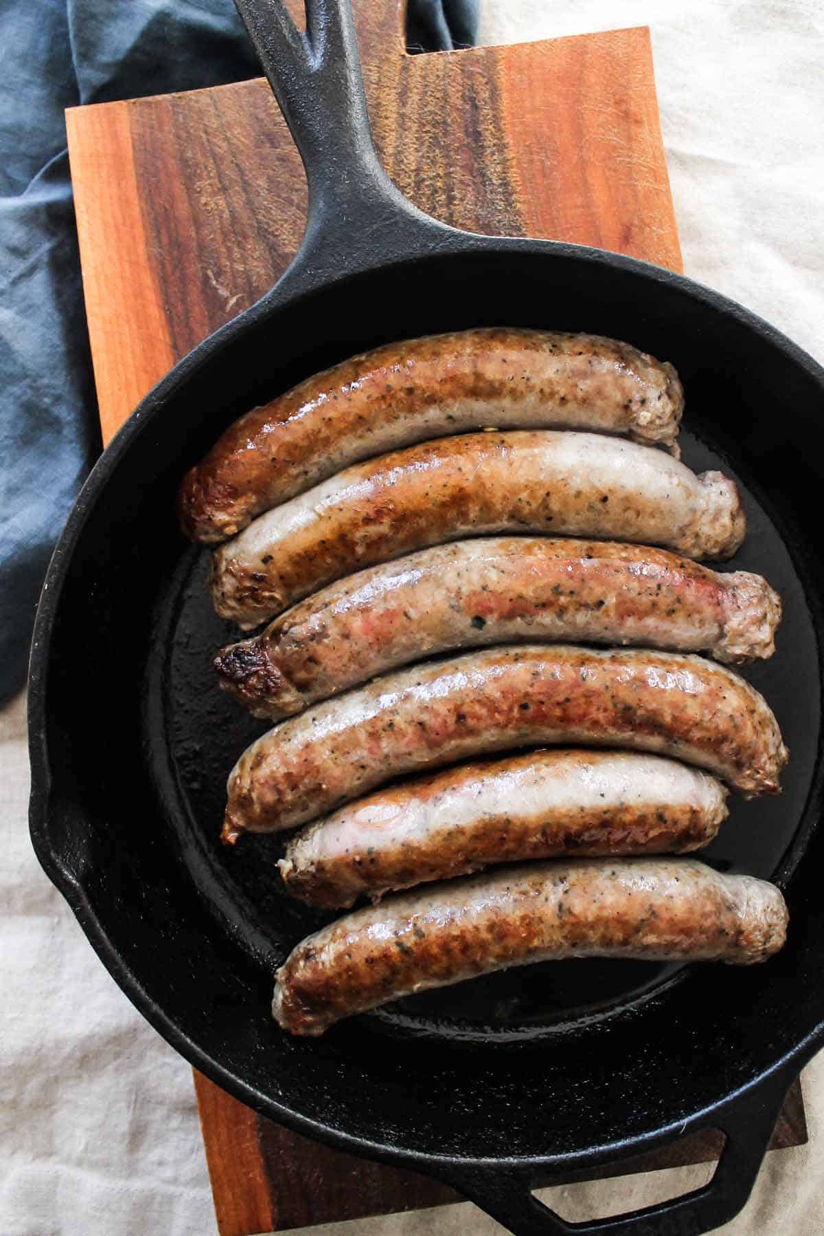 Overhead Shot Of Browned Sausages In Skillet On Wooden Board