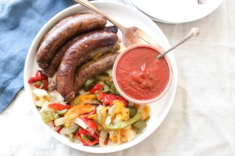 Overhead Shot Of Crock Pot Sausages With Peppers And Onions In Bowl on Tablecloth