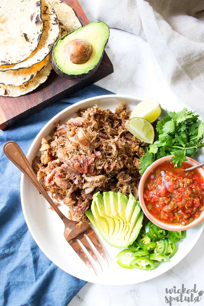 crispy carnitas on a plate with sliced avocado and fresh lime