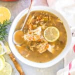 A bowl of soup with chicken and lemon with lemons scattered around.