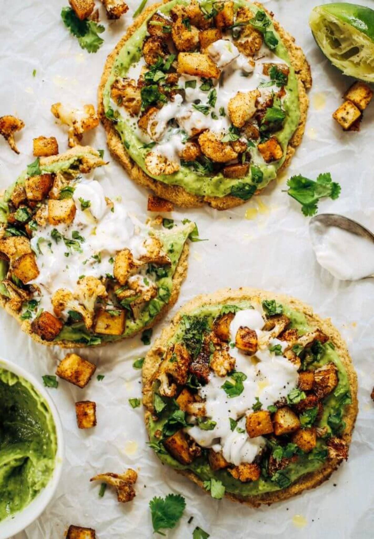 3 cauliflower pittas topped with guacamole, herbs, and roasted cauliflower cubes