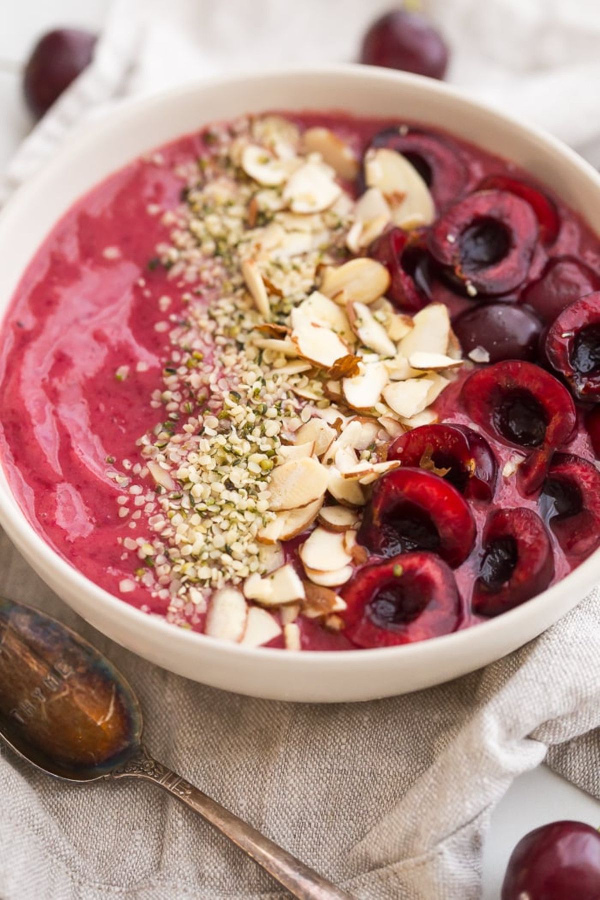 A bowl of cherry smoothie, sliced almonds and whole cherries