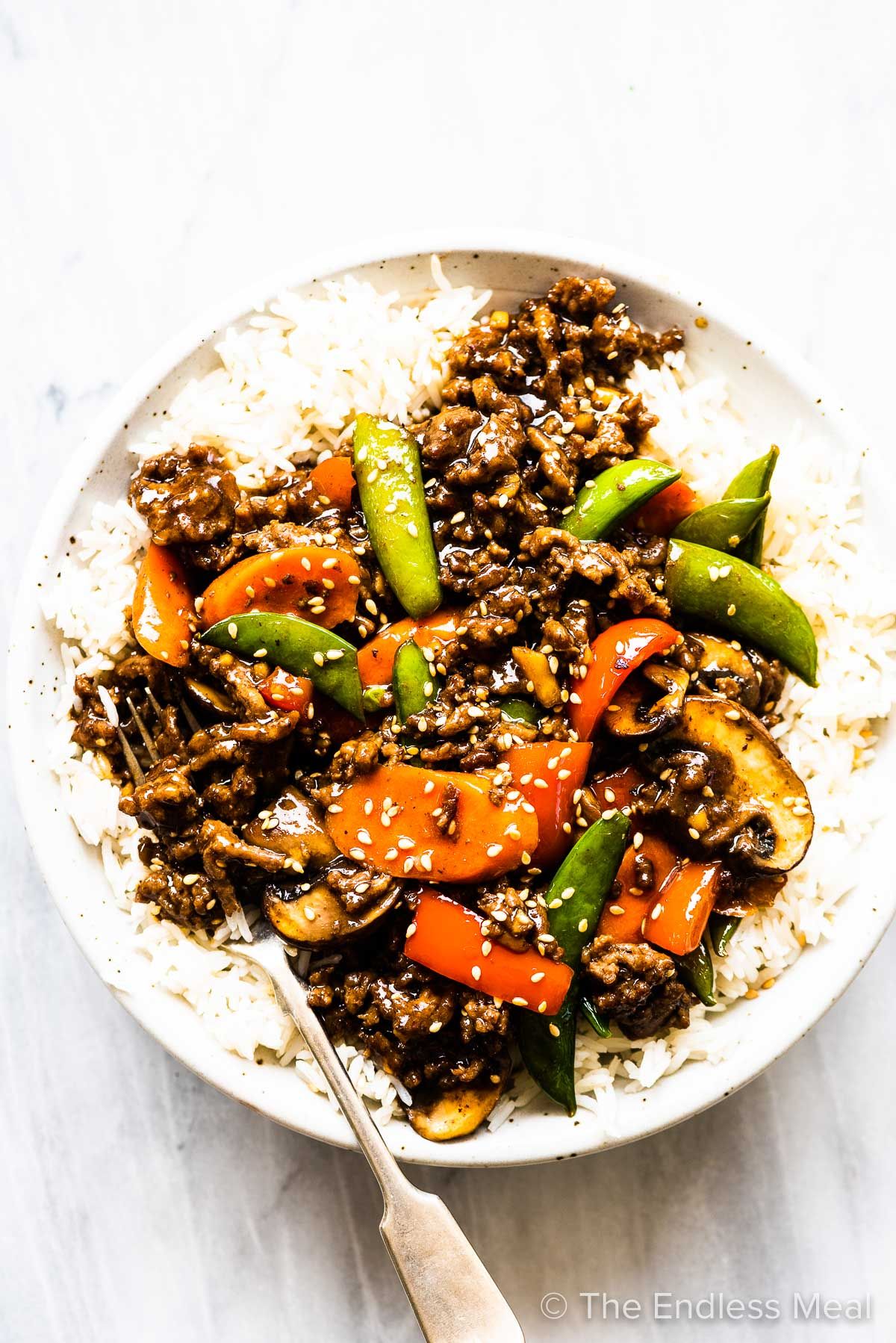 A bowl of beef and vegetable stir fry with a fork on one side of it