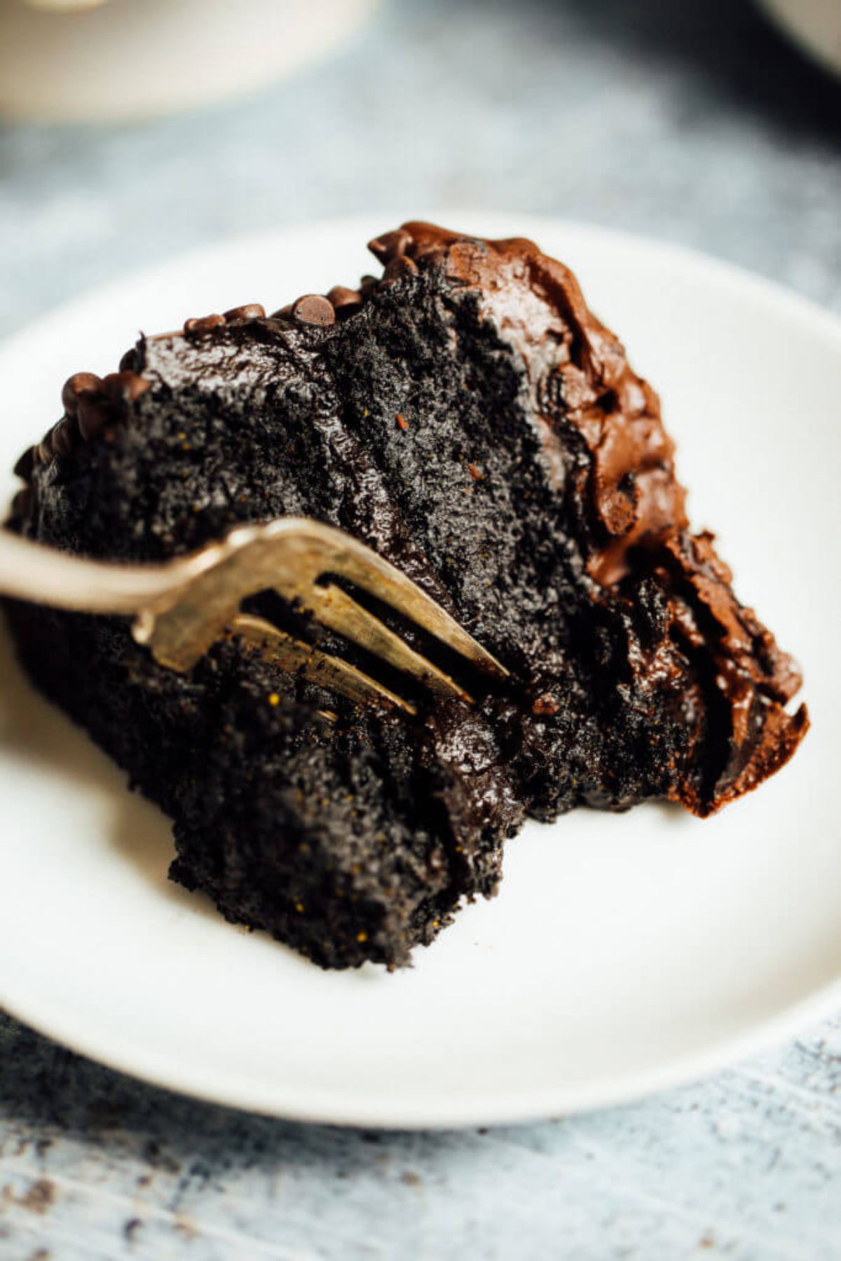 A white plate with a portion of chocolate cake on it, a fork resting in the slice