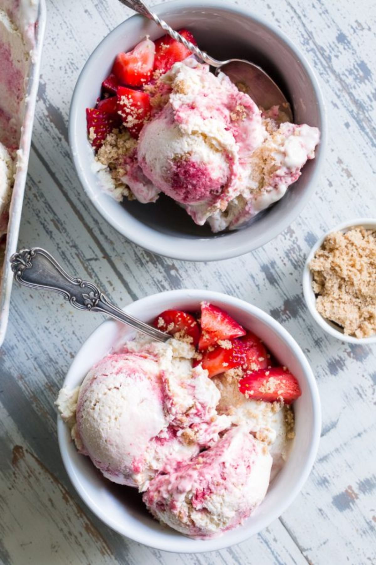 2 bowls of strawberry cheesecake ice cream with spoons sticking out of them, topped with fresh strawberries