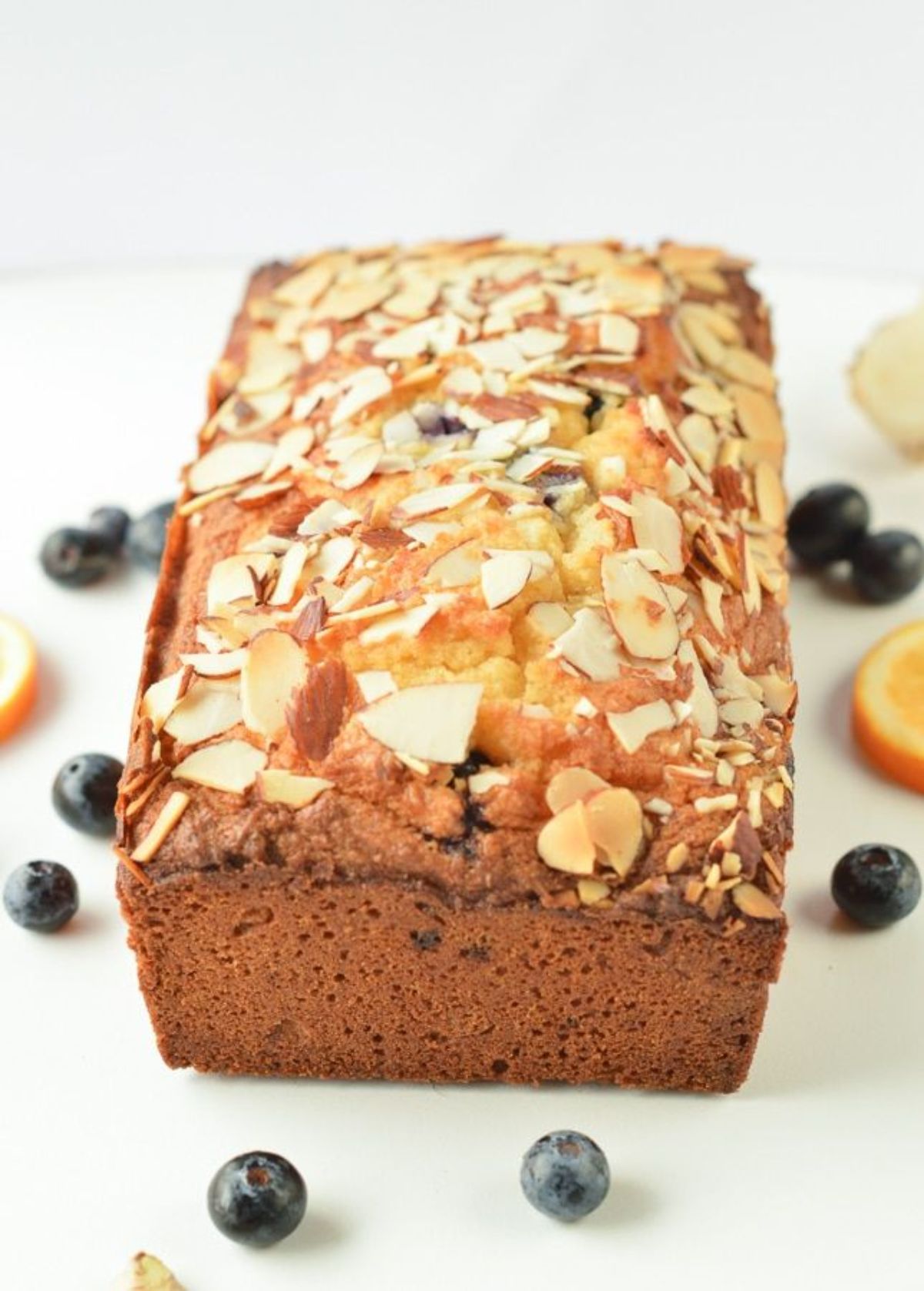 A loaf of blueberry bread topped with sliced almonds and blueberries scattered around it