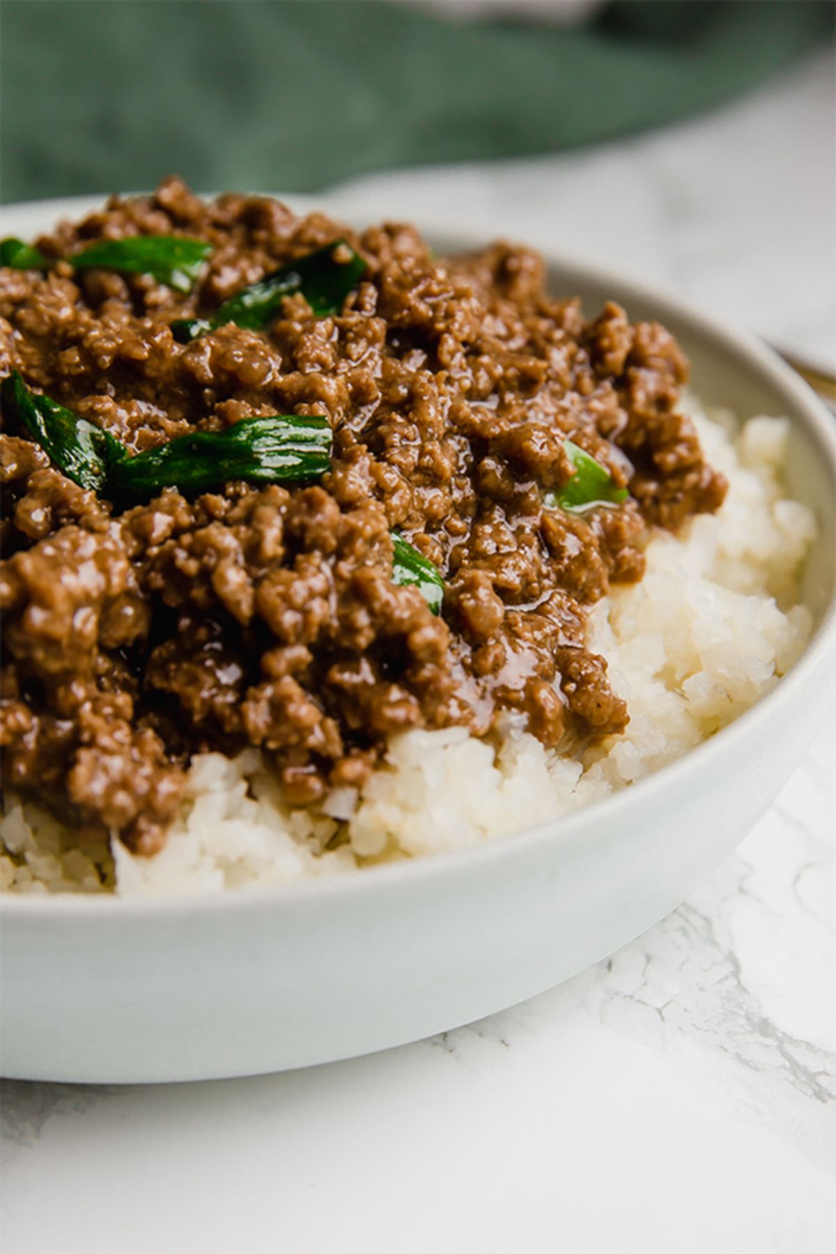 A white bowl of ground beef in sauce on top of rice