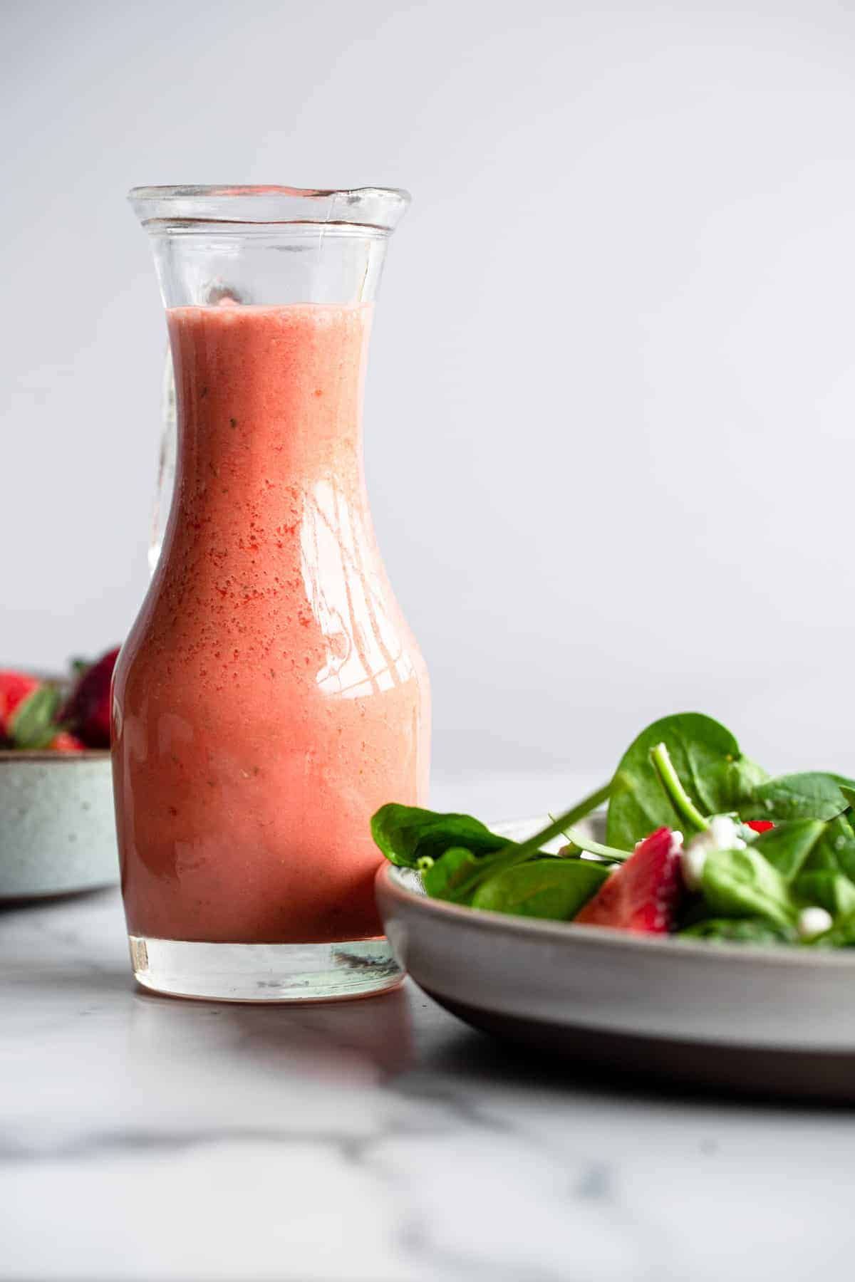 A tall jar of red dressing next to a plate of salad