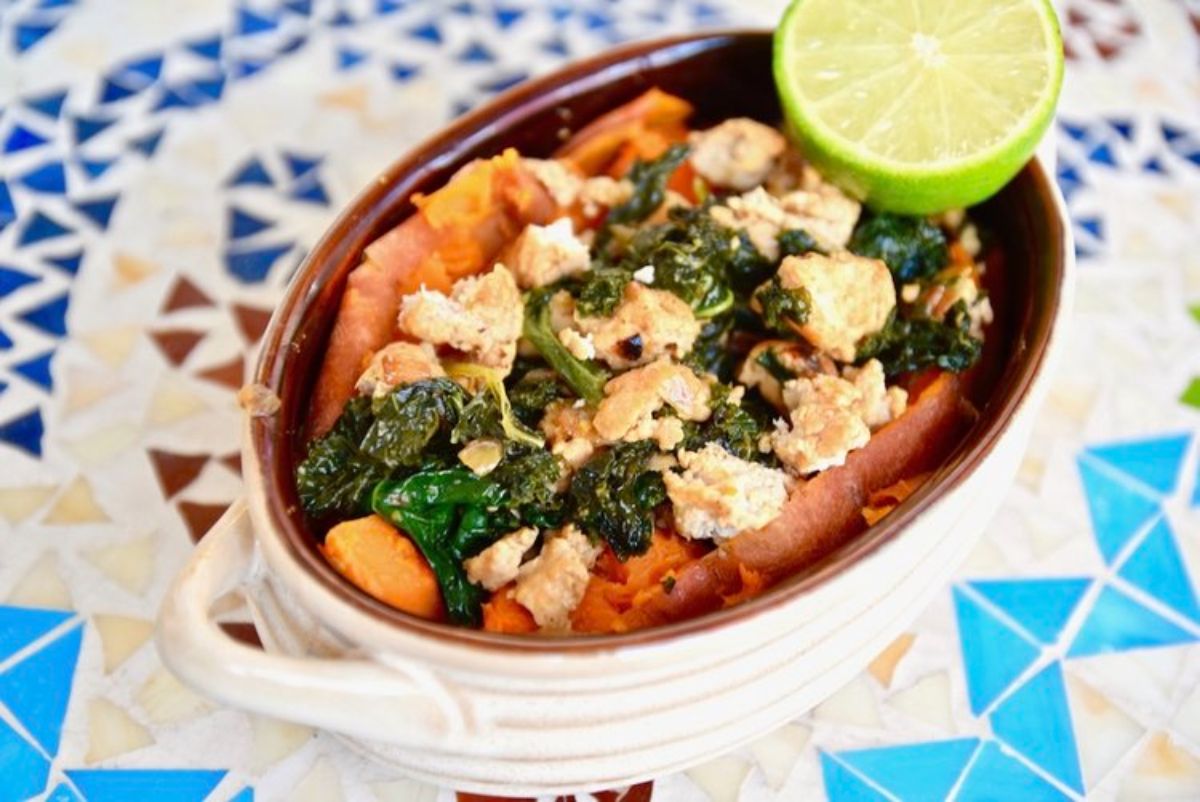 An oval casserole dish containing a sweet potato stuffed with ground turkey and kale