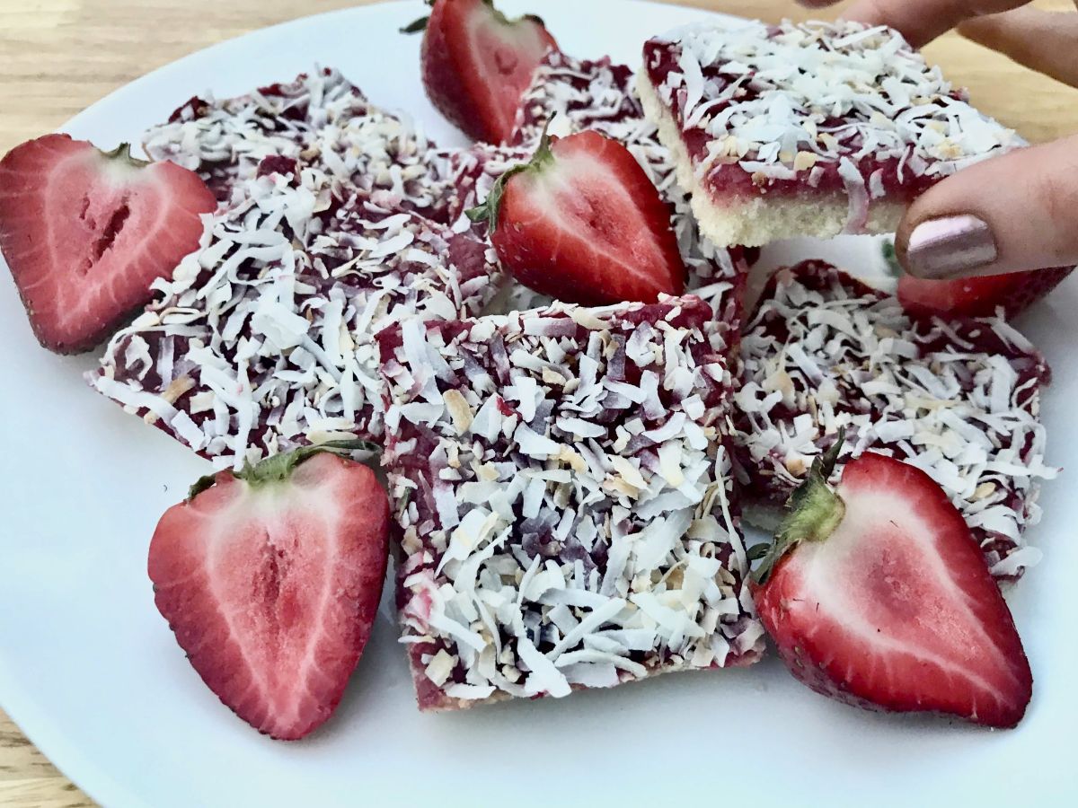 A plate of strawberry coconut bars surrouned by halved strawberries