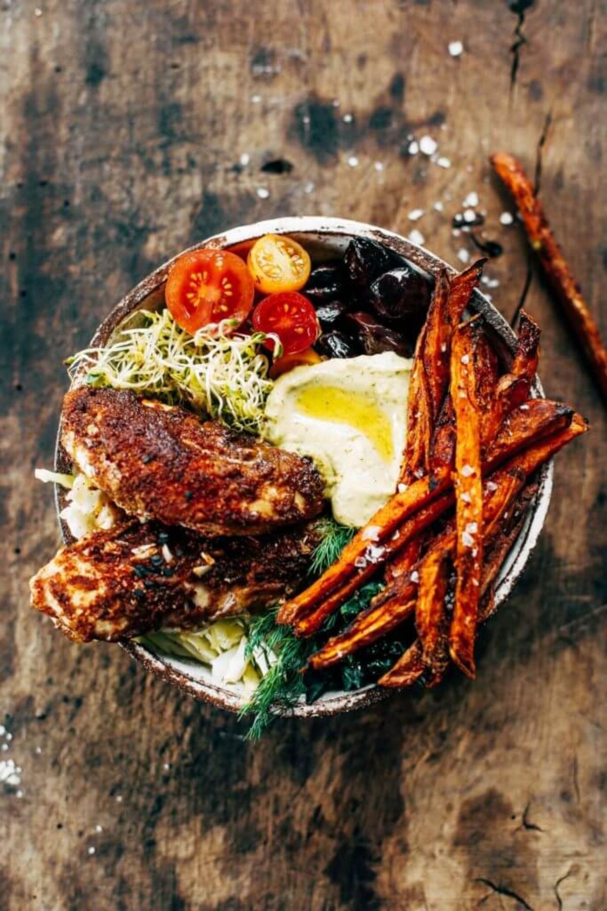 A bowl of chicken, swett potato fries, tomatoes and olives