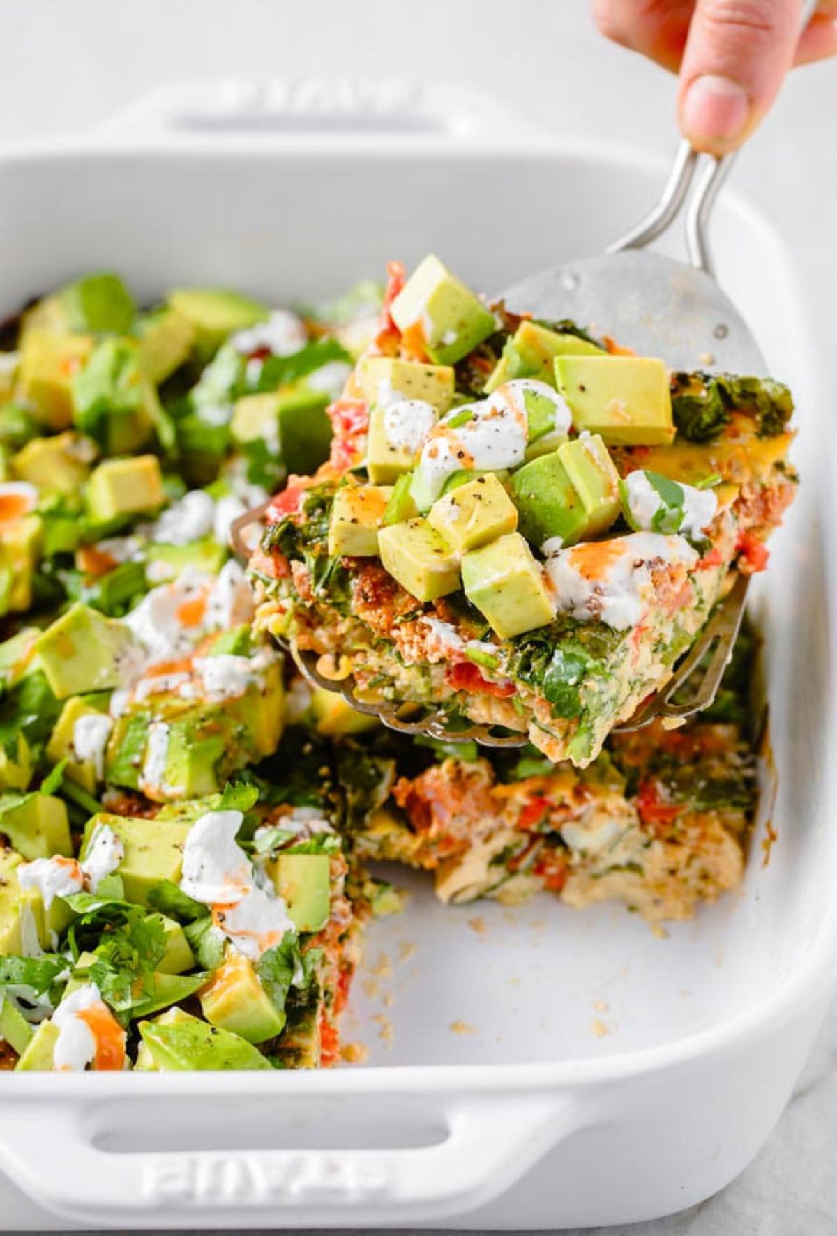 A white casserole dish filled with avocado casserole. A fish slice is lifting out a portion