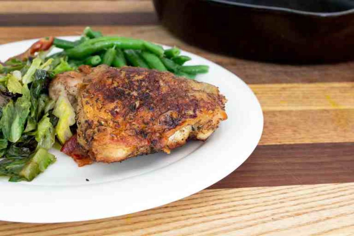 a white plate with a chicken thigh, green beans and sliced greens