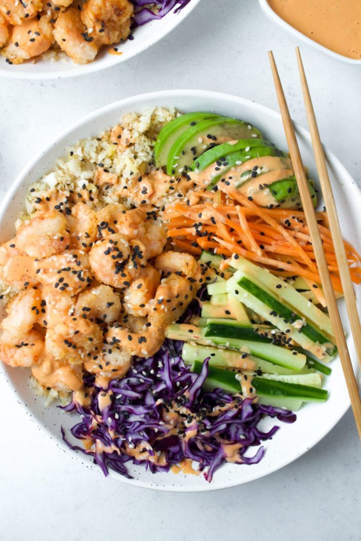a white bowl of shrimp, sliced red cabbage, matchstick cucumbers and carrots, and sliced green apple. Chopsticks are resting on the side of the plate