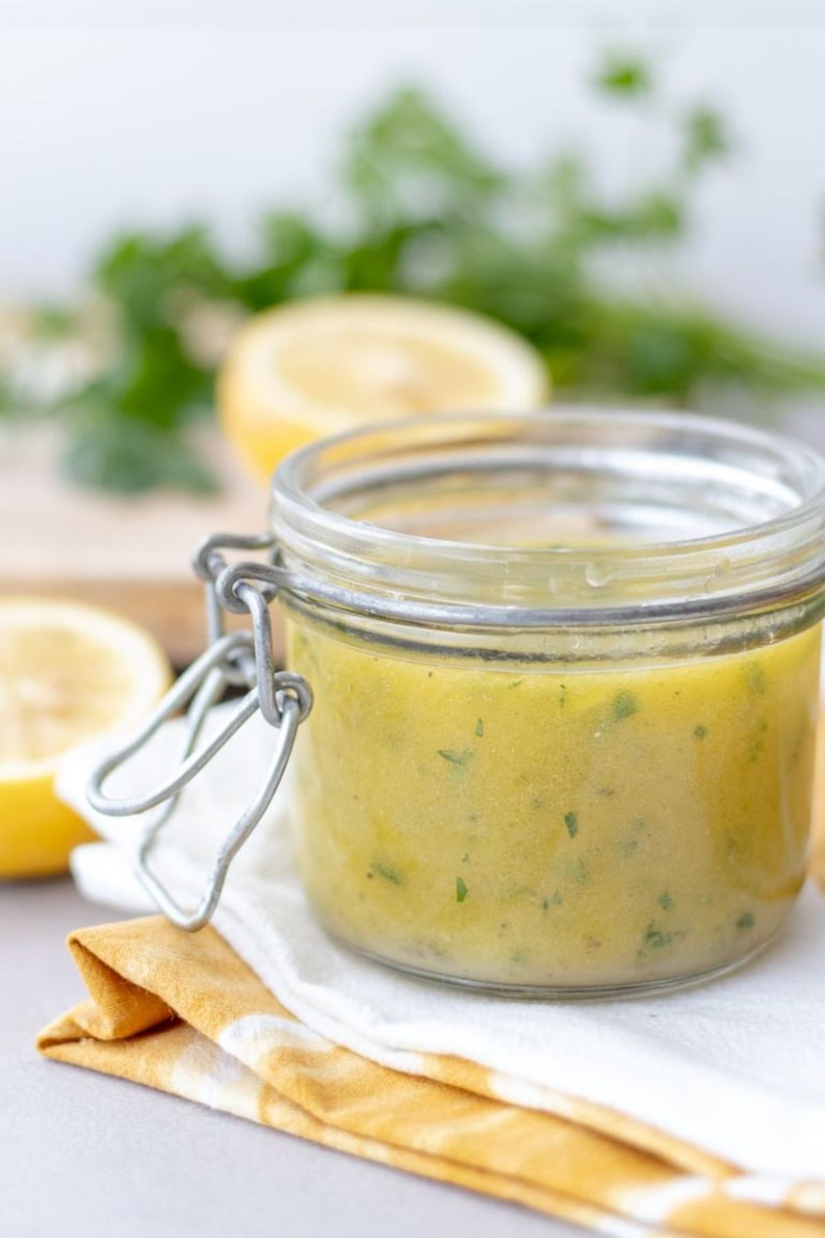 A kilner jar with clip full of lemon herb vinaigrette with lemons and hebrs just seen in the background