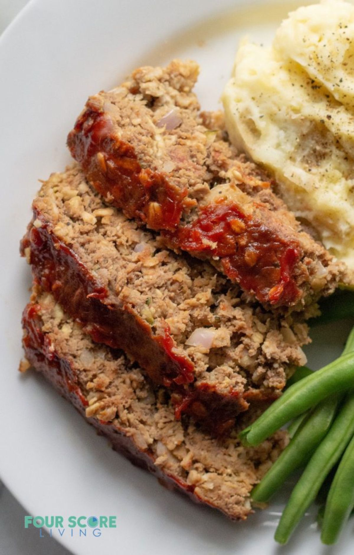 A white plate with slices of meatloaf, green beans and mash on it