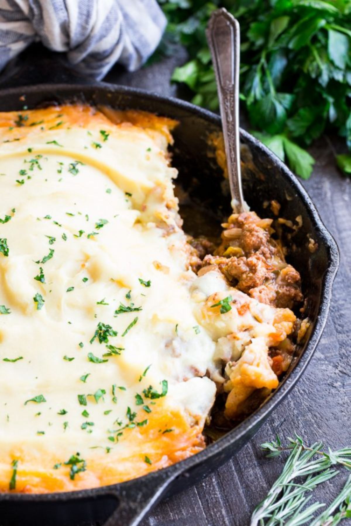 a cast iron skillet filled with shepherd's pie. A spoon is scooping out a portion