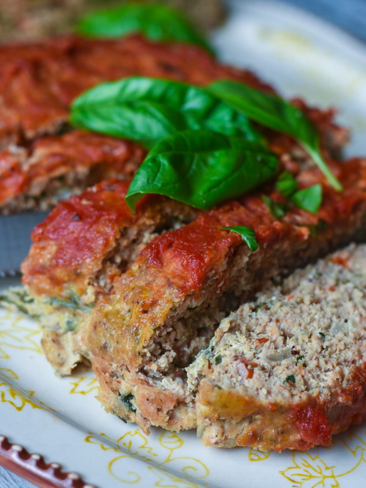 A partial shot of a platter with slices of meatloaf on it, topped with basil leaves