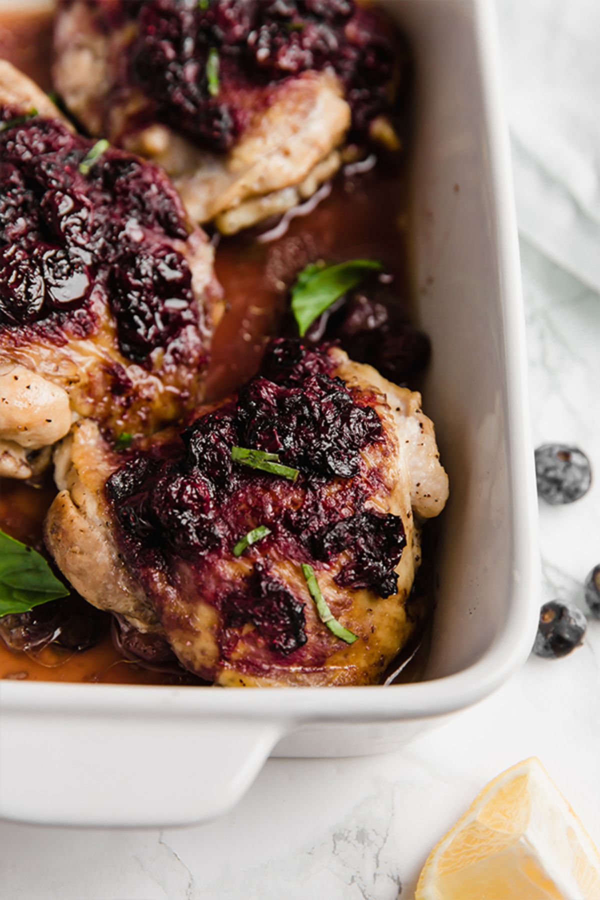 a partial shot of a casserole dish with roast chicken thighs, topped with bluberry balsamic marinade