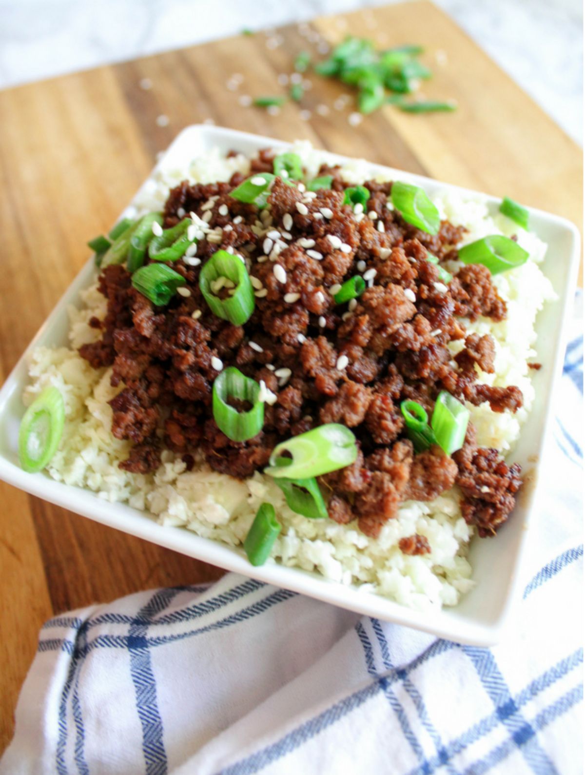 a square bowl of rice with ground beef on top sprinkled with scallions and sesame seeds