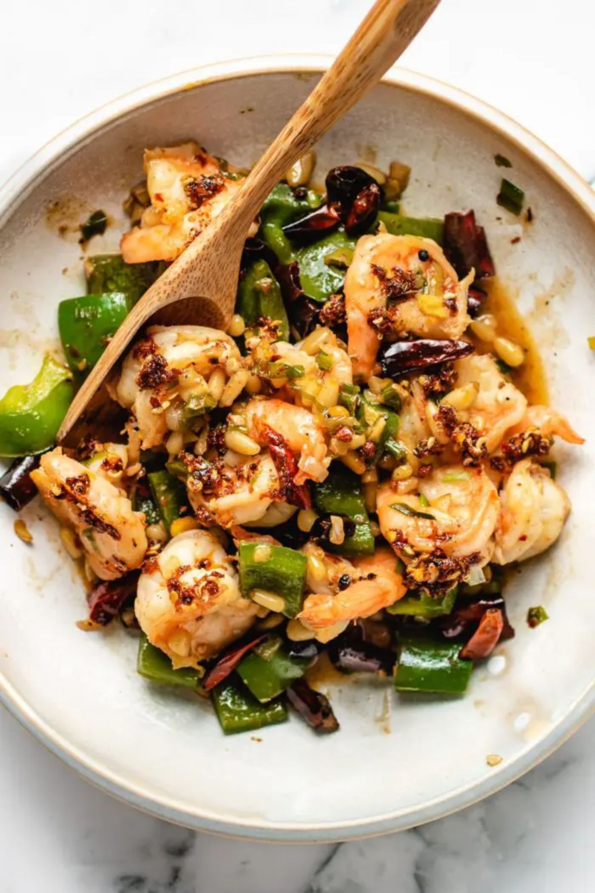 a white bowl of shrimp, pine nuts, scallions and herbs with a wooden spoon