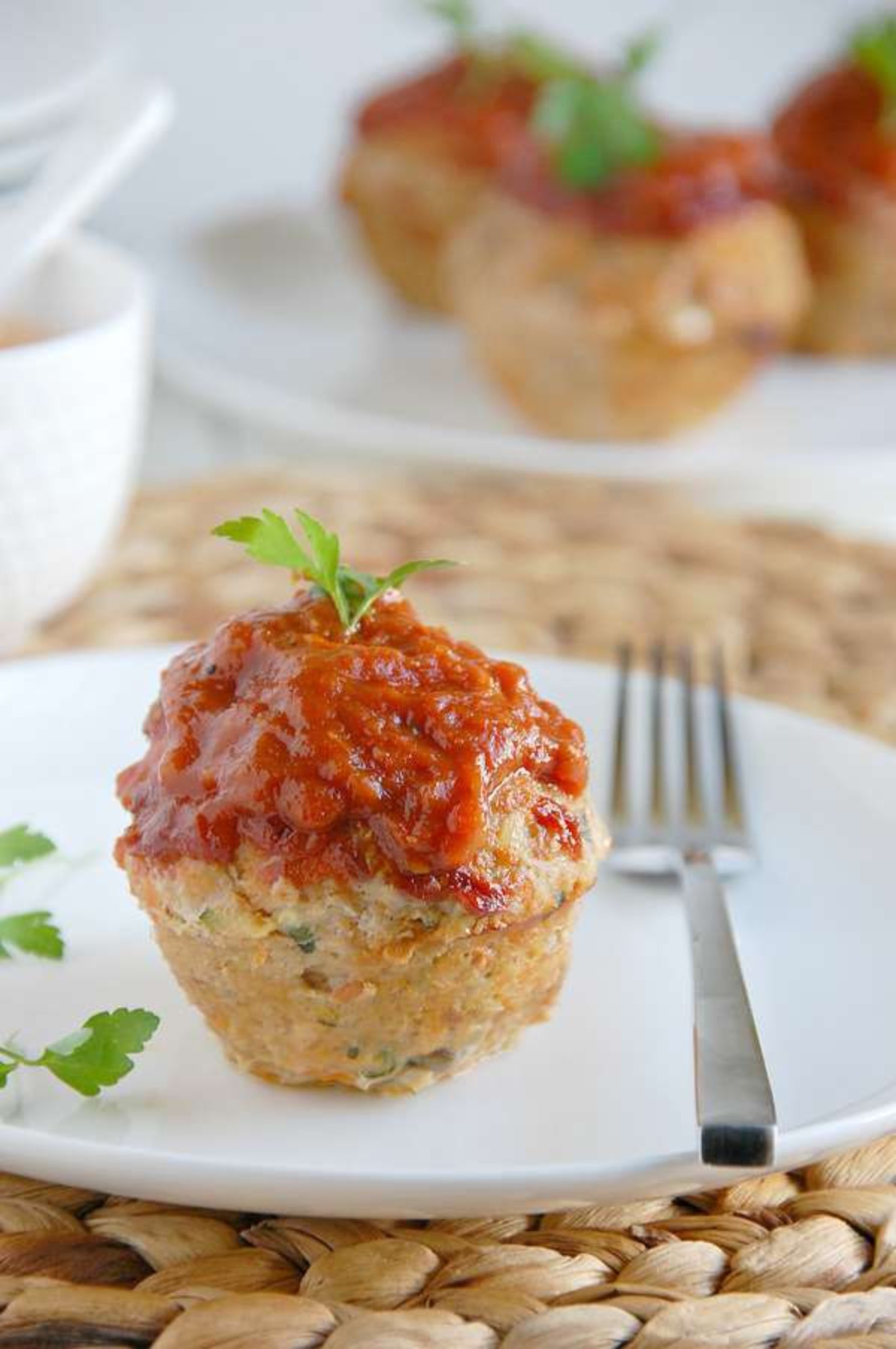 a white plate with a small turkey and vegetable muffin on it, topped with tomato sauce and sitting next to a silver fork