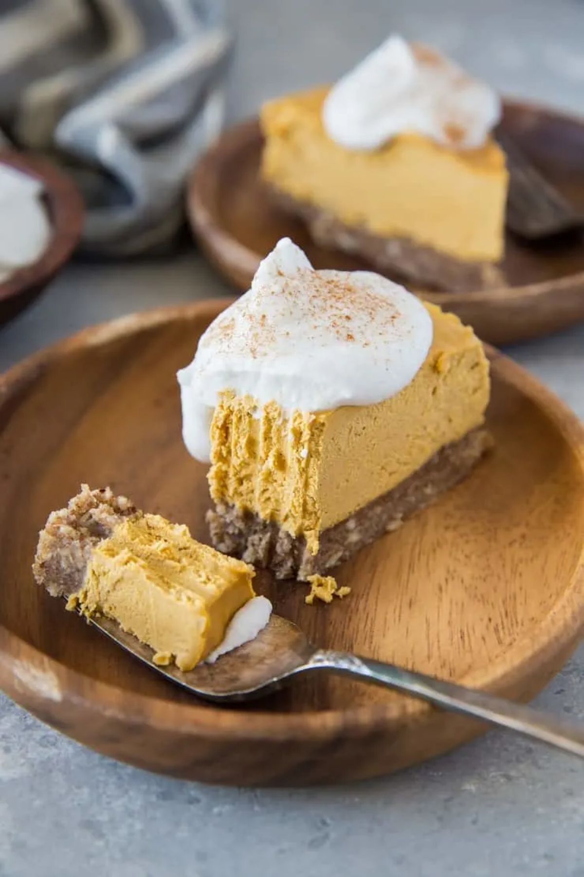 A wooden plate with a pumpkin cheesecake on it, topped with cream