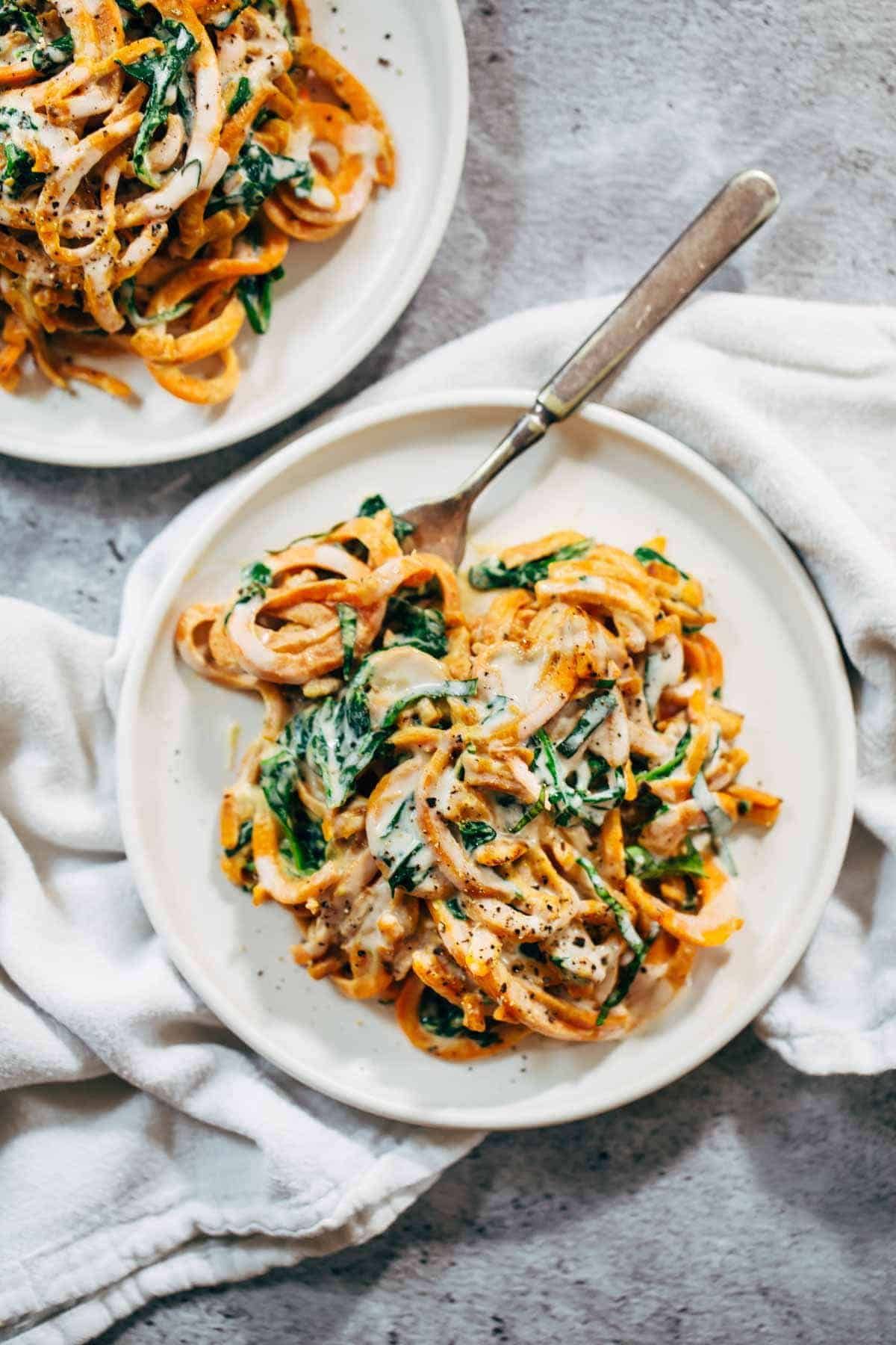 2 white plates of sweet potato noodles and spinach in a creamy sauce