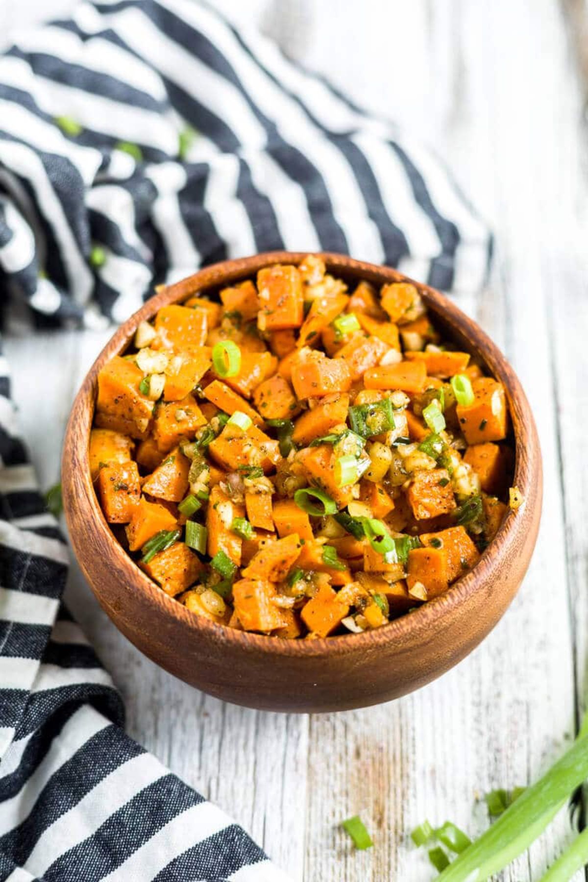 a wooden bowl of sweet potato salad on a worktop with a striped cloth