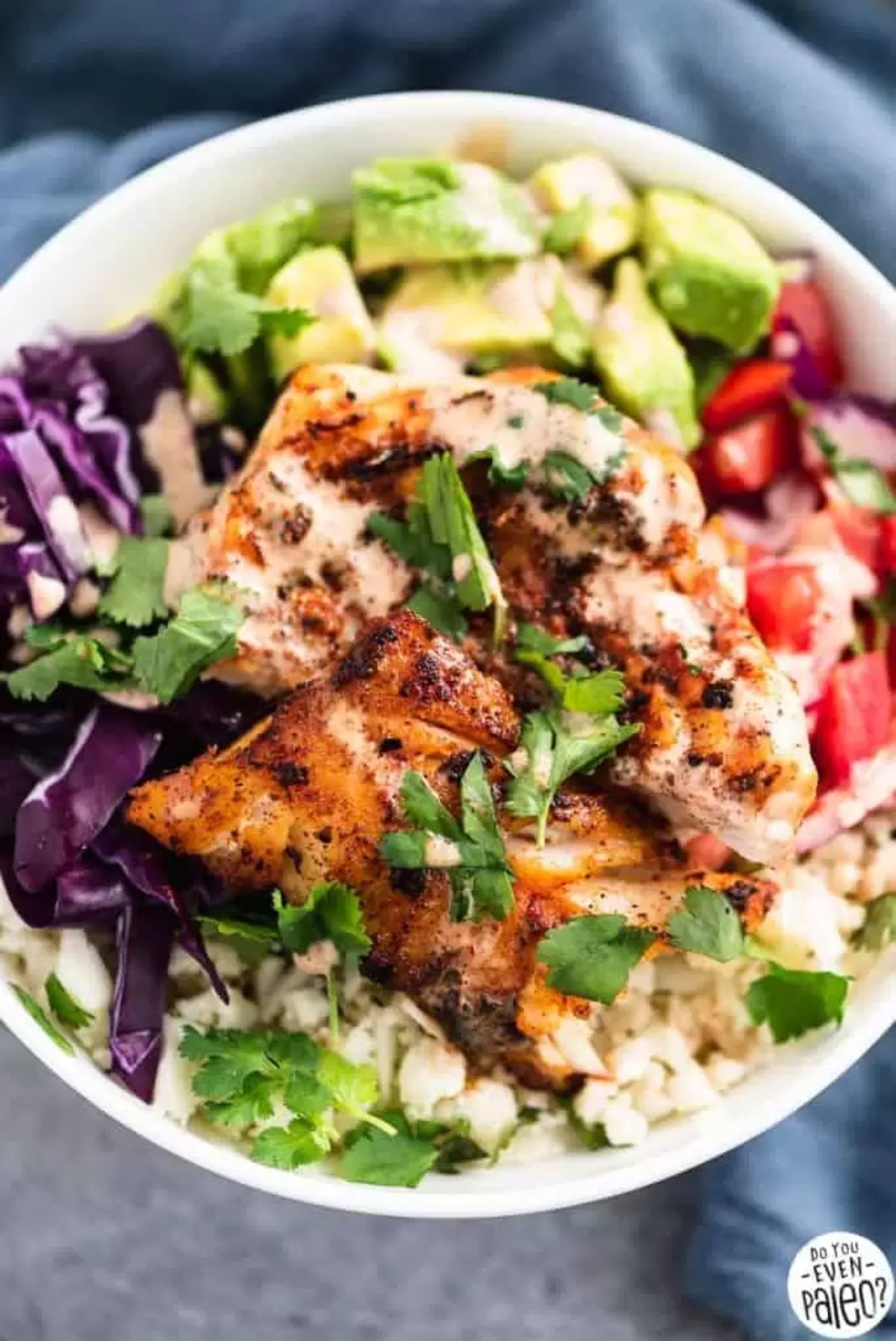 a bowl of fish, red cabbage, avocade, tomatoes and fish fillet, topped with chopped herbs