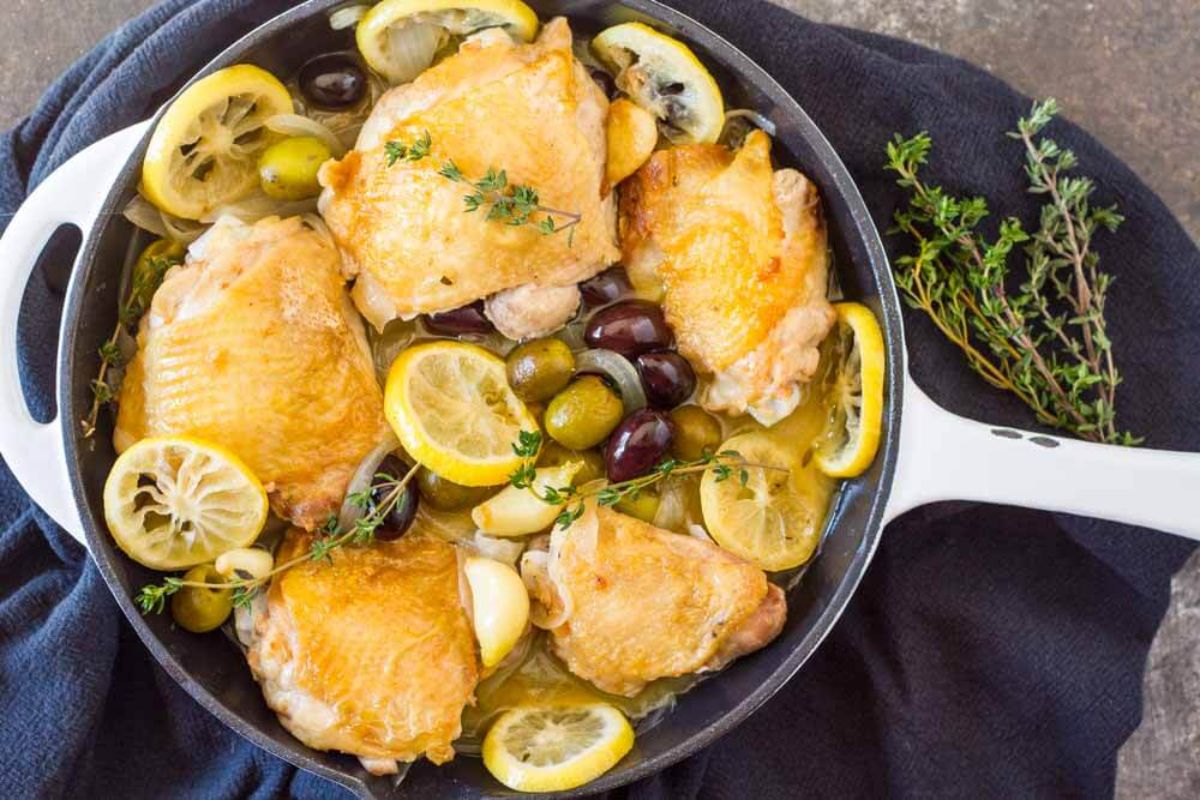 a skillet with chicken thighs, lemon slices and olives