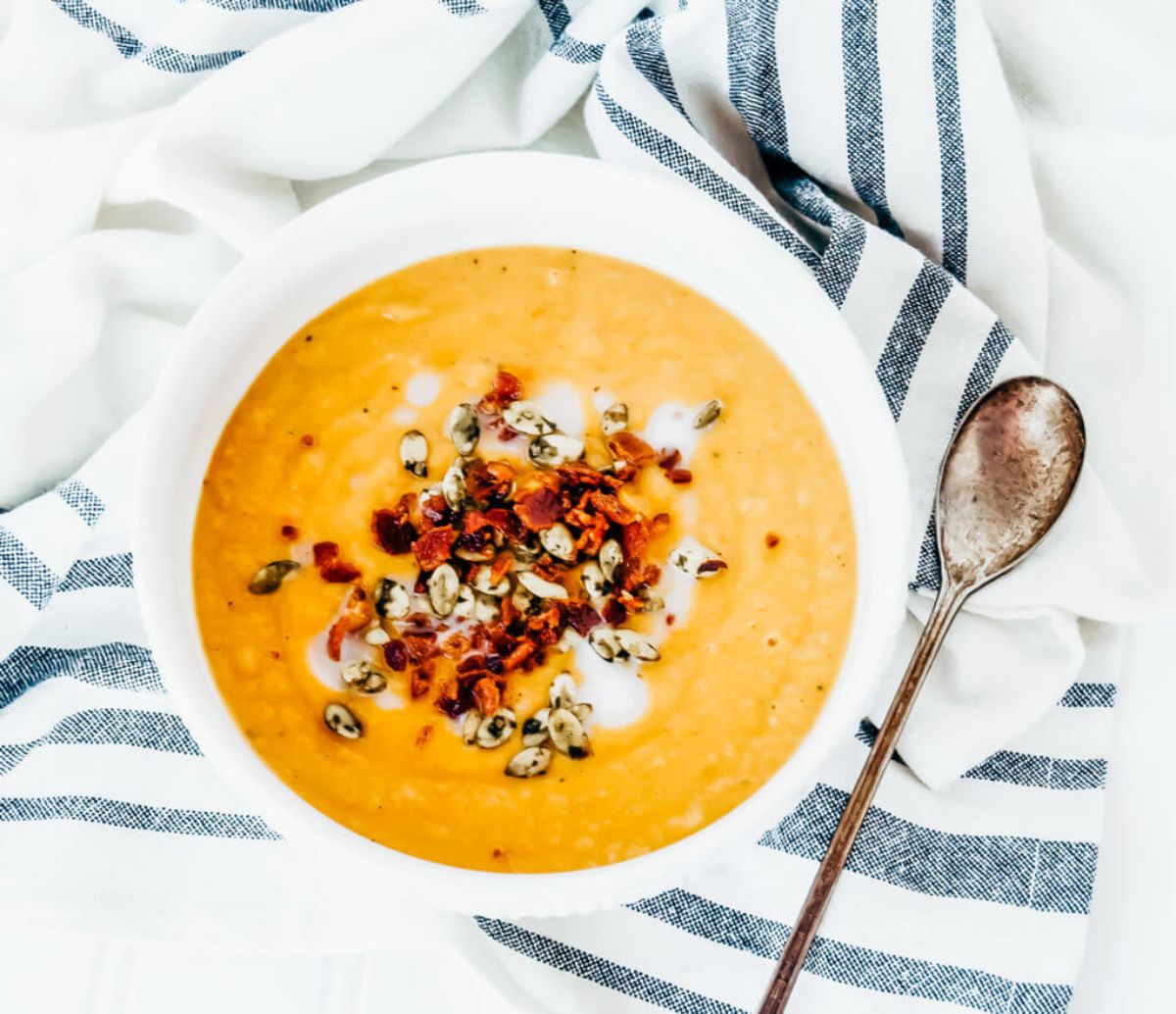 a bowl of butternut squash soup topped with toasted seeds and bacon bits