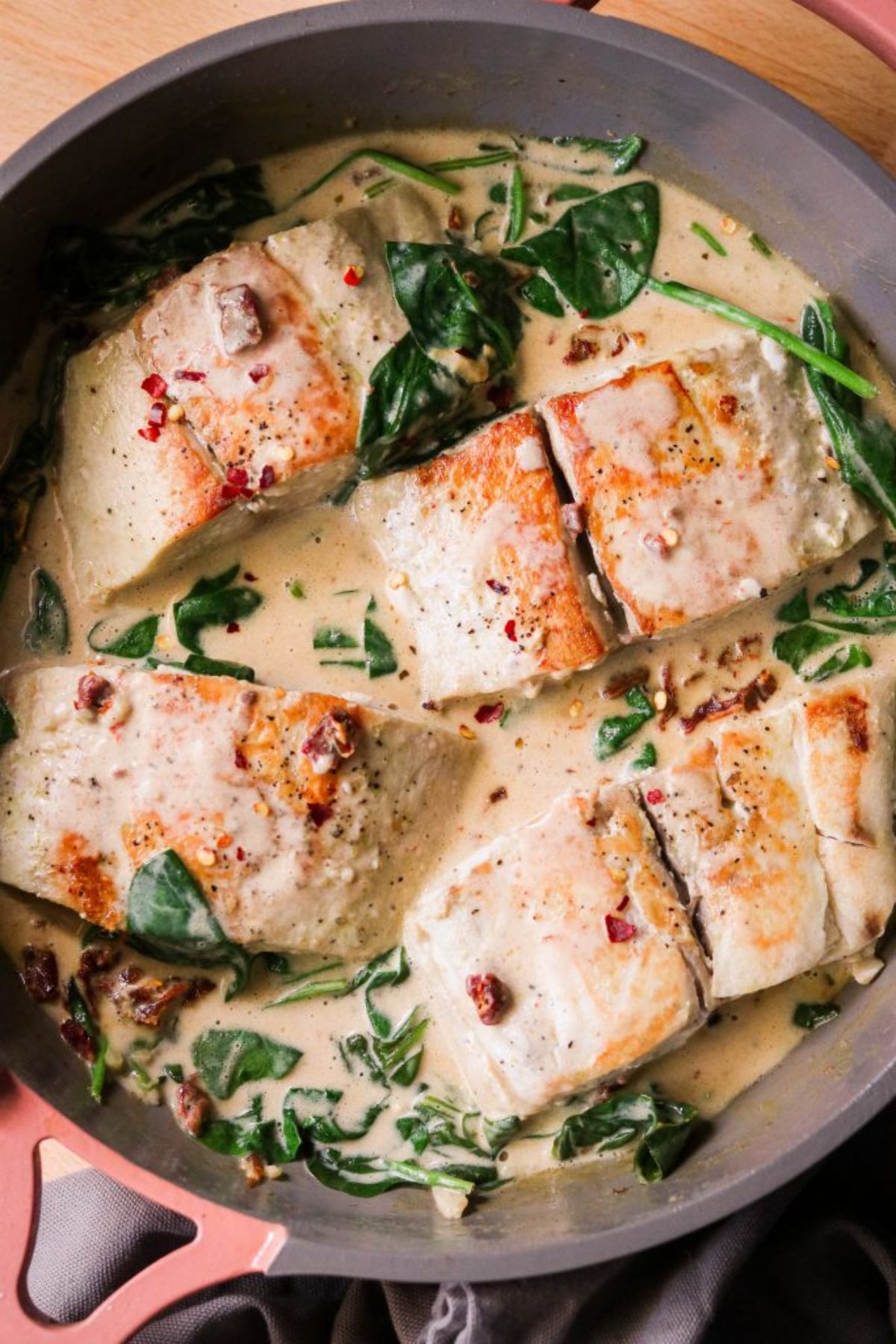 a skillet of slamon fillets in a creamy spinach sauce