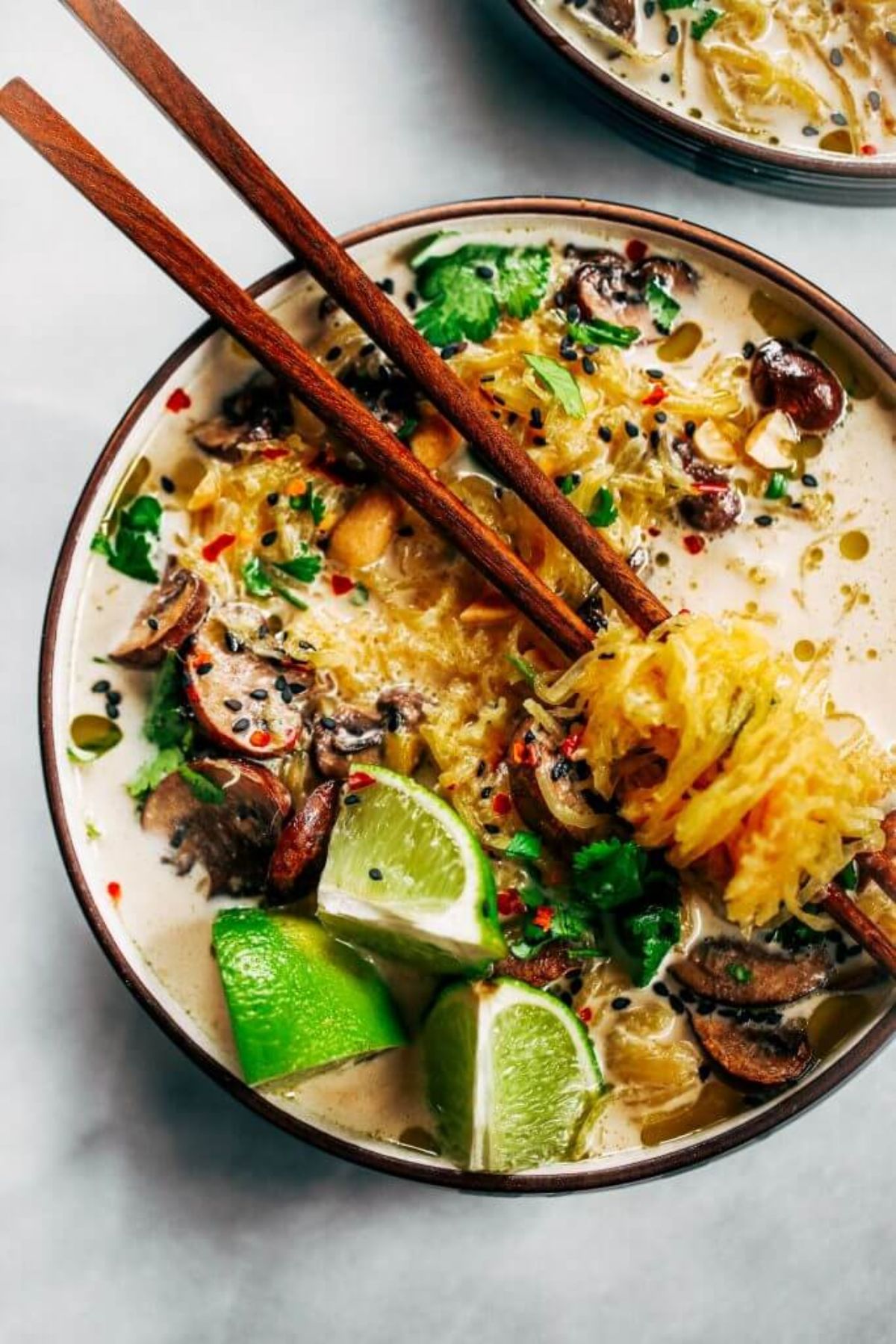 A bowl of spaghetti squash noodles and lime wedges with chopsticks resting on it