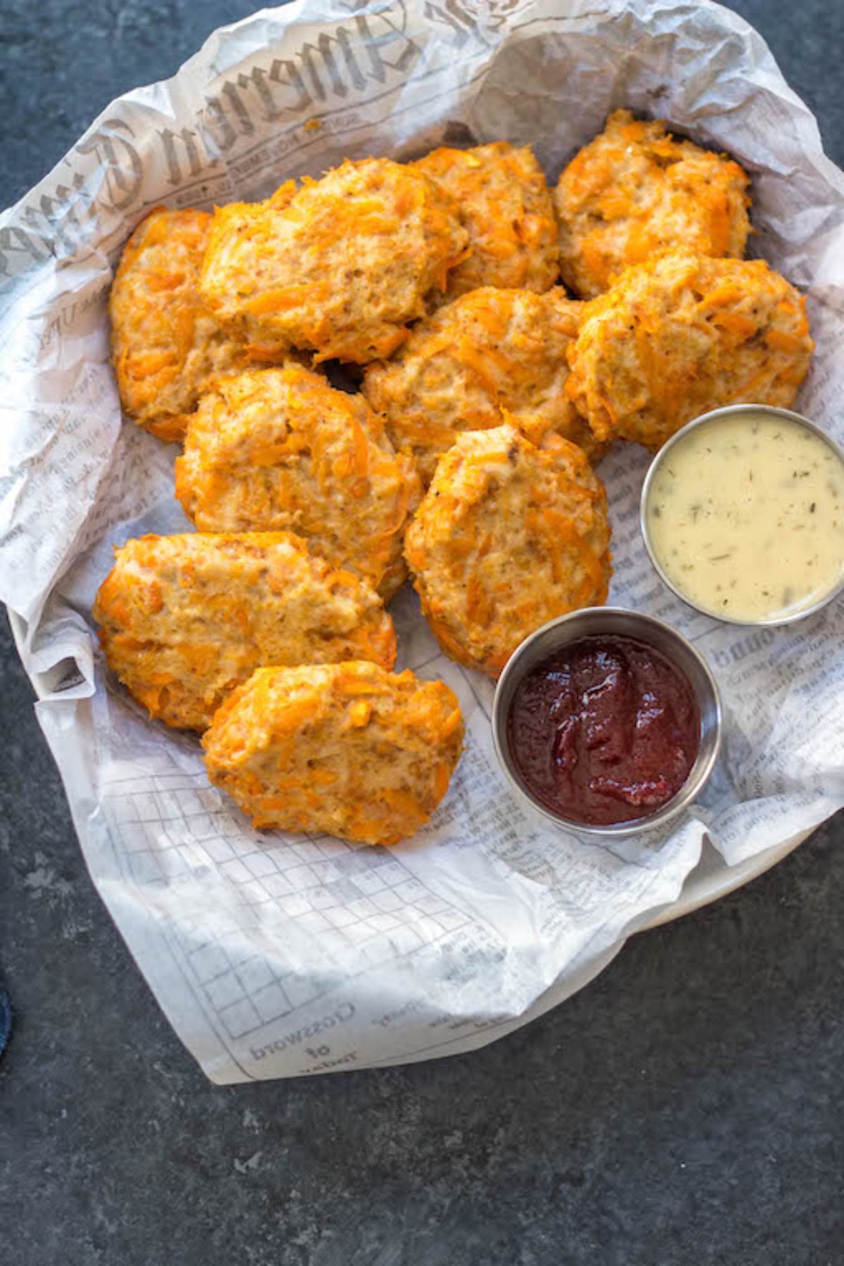 a paper lined bowl of chicken nuggets next to small bowls of white and red sauce