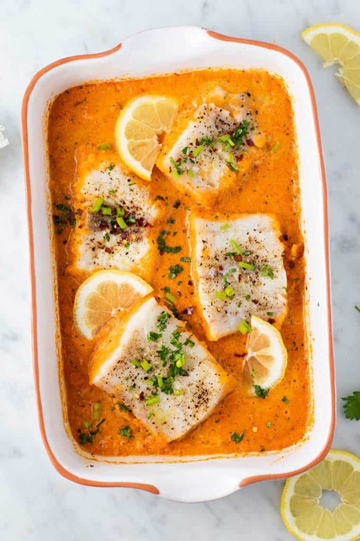 a casserole dish with baked cod fillets in red pepper sauce.