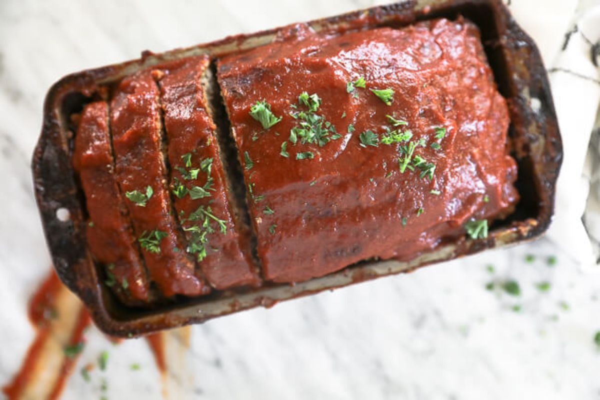 a loaf tin full of meatloaf topped with sauce and chopped herbs