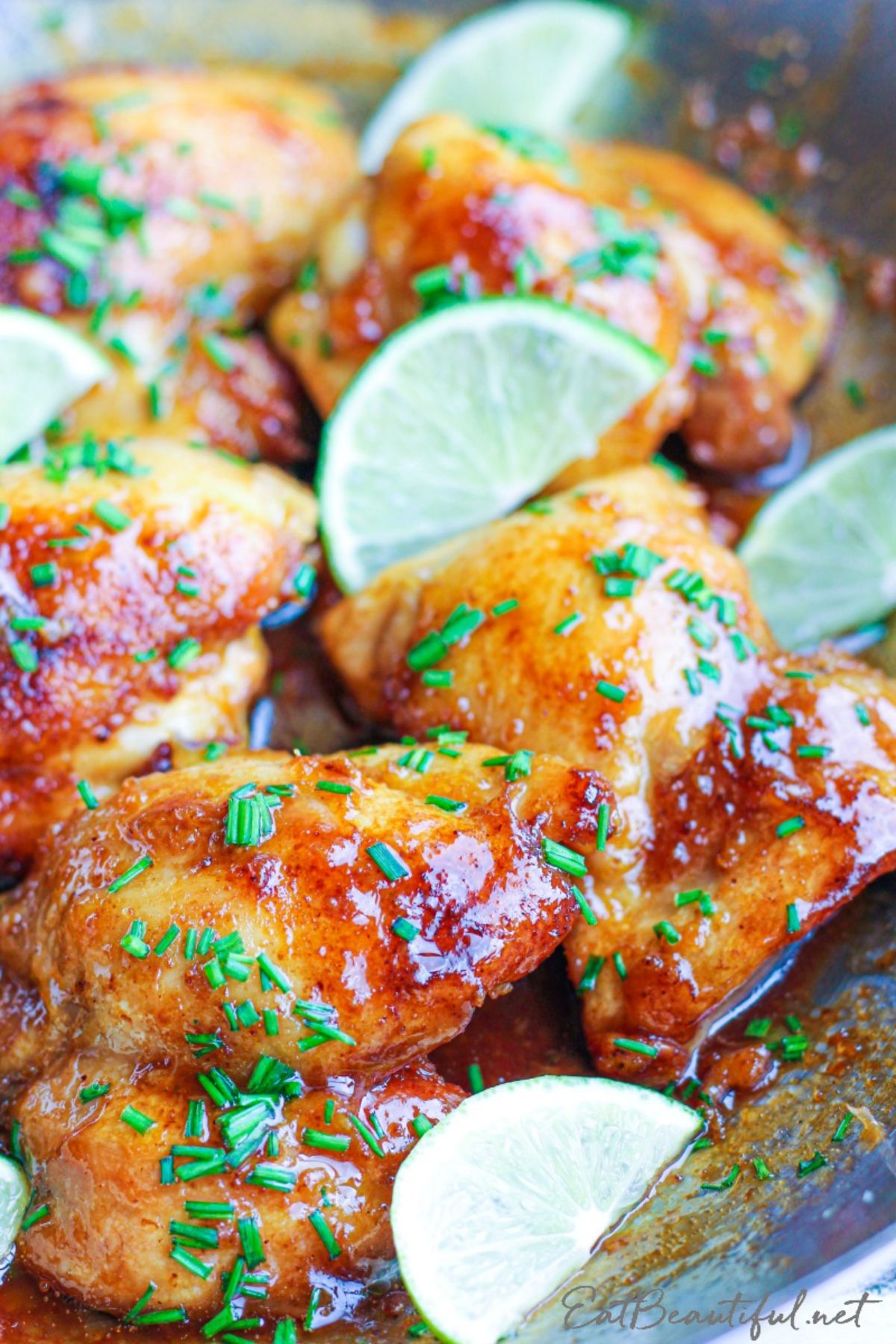 a partial shot of a bowl with marinaded chicken thighs garnished with lime wedges and chopped herbs