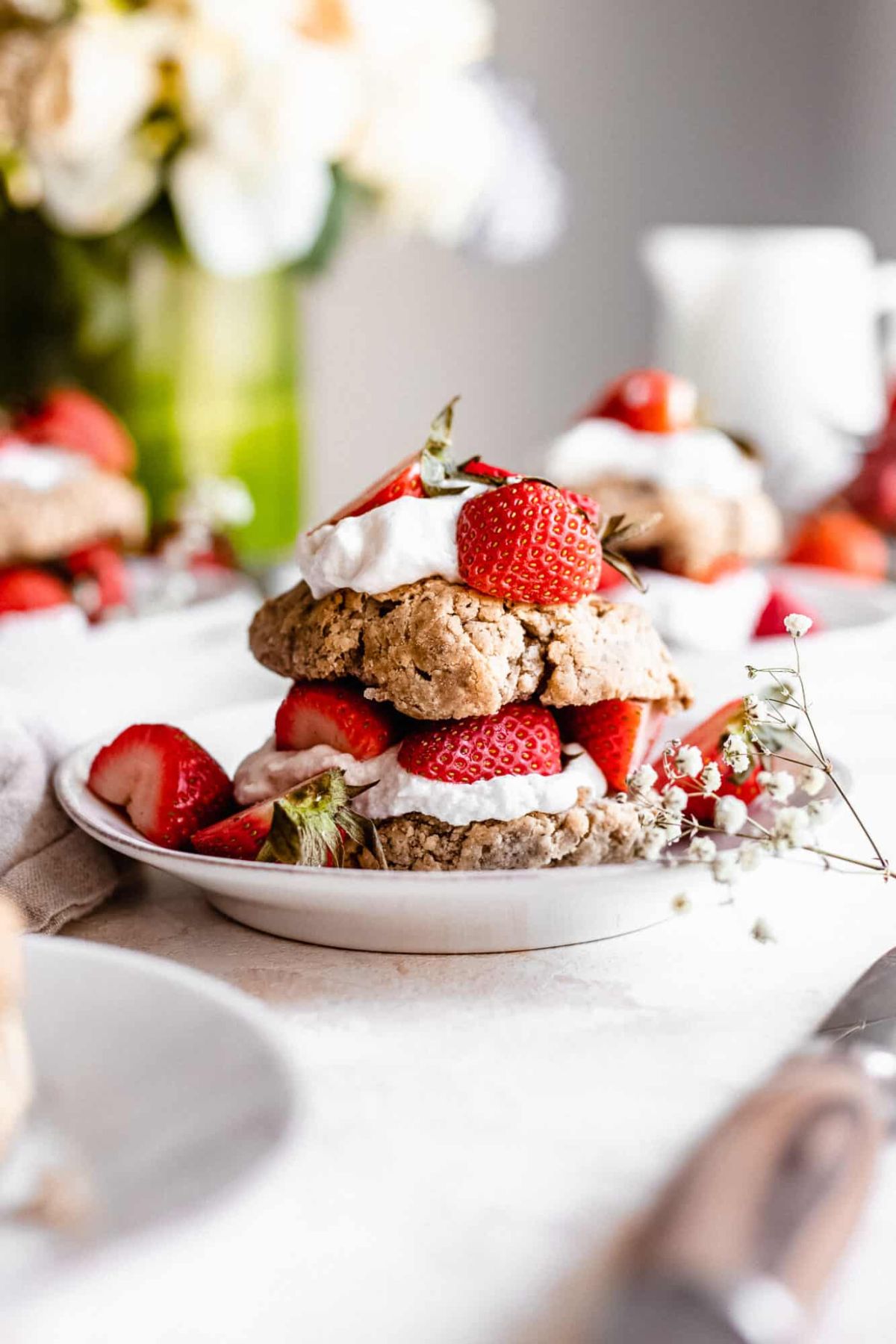 a plate holding a stack of strawberry shortcake biscuits, sandwiched with fresh strawberries and cream