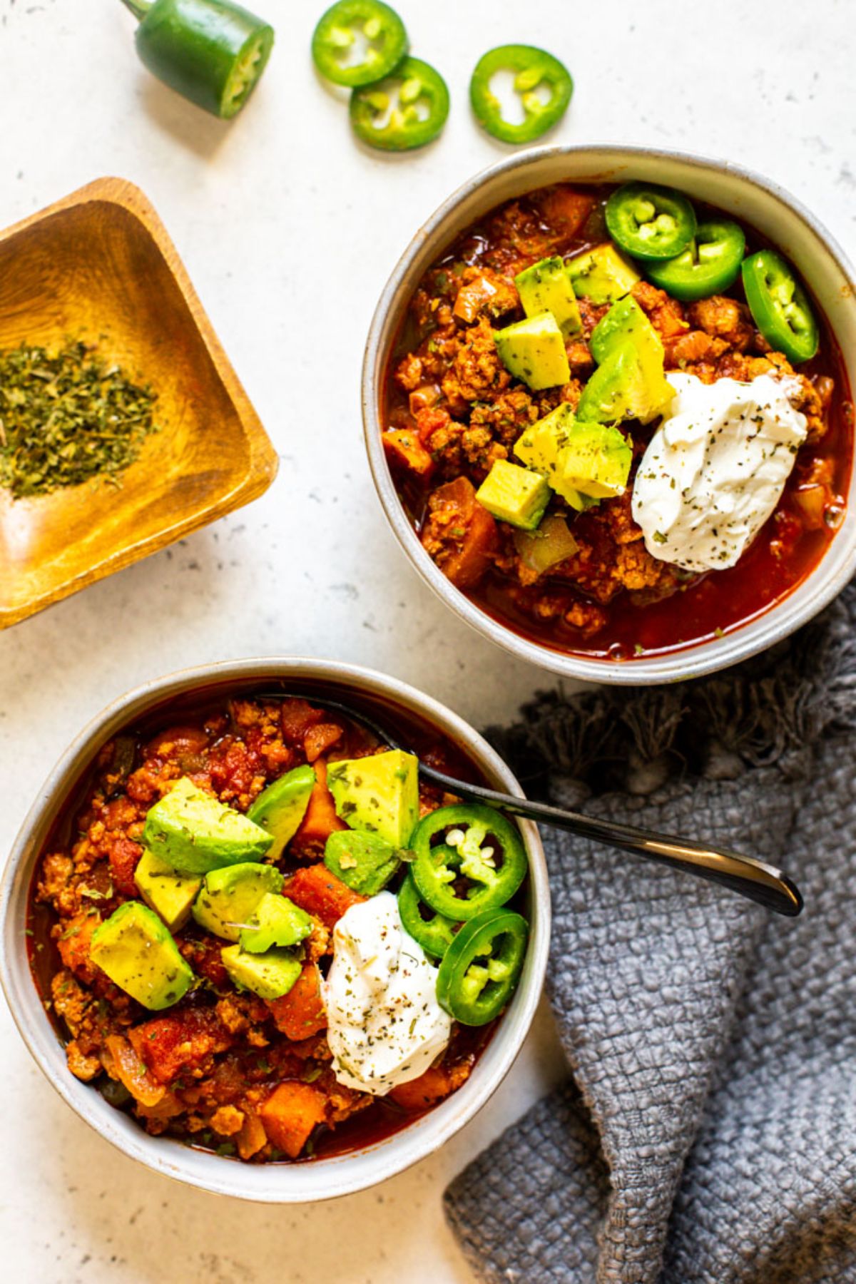 2 bowls of turkey chilli topped with avocado, sliced Jalapenos and sour cream.
